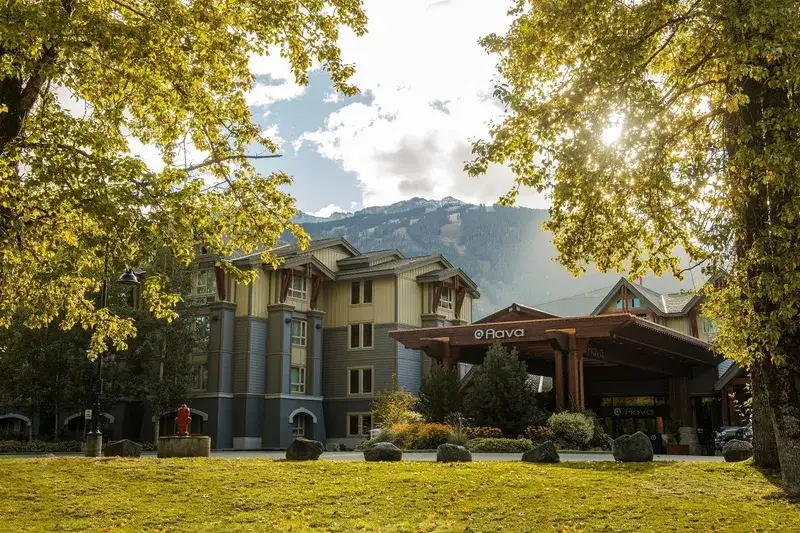 The Aava Whistler Hotel entrance framed by autumn trees with the mountains behind