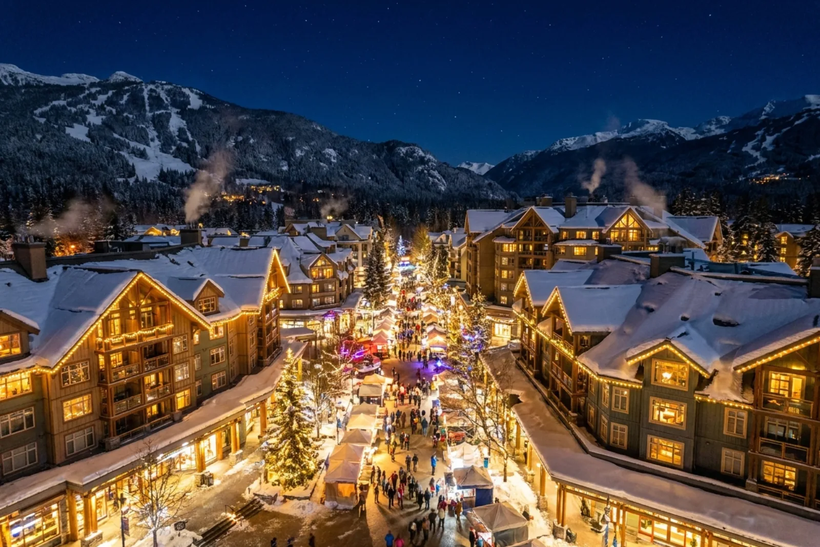 Aerial view of Whistler Village at night, lit up for winter, with snowy mountains behind